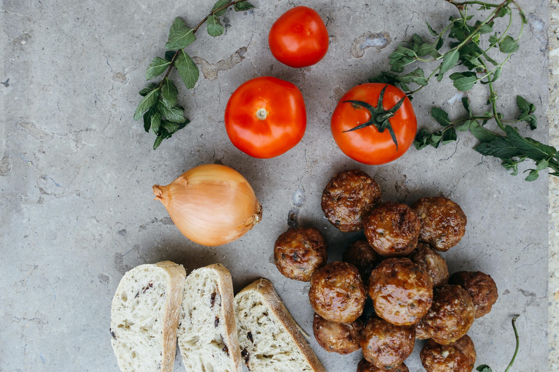 Top-down view of ingredients for a delicious sandwich with bread, meatballs, onions, tomatoes, and herbs.